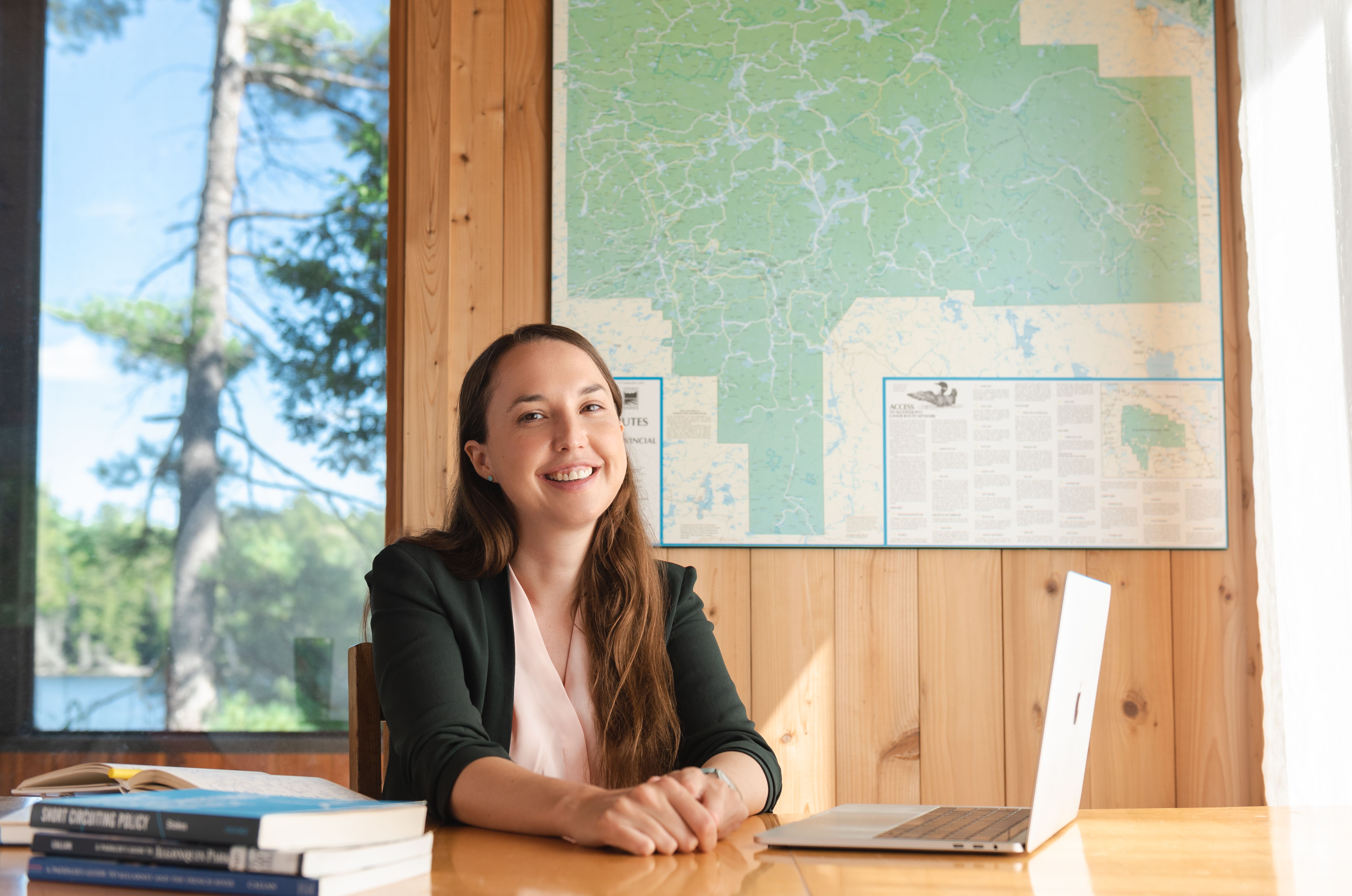 Photo of Leah Stokes sitting in front of a laptop with a window behind her 